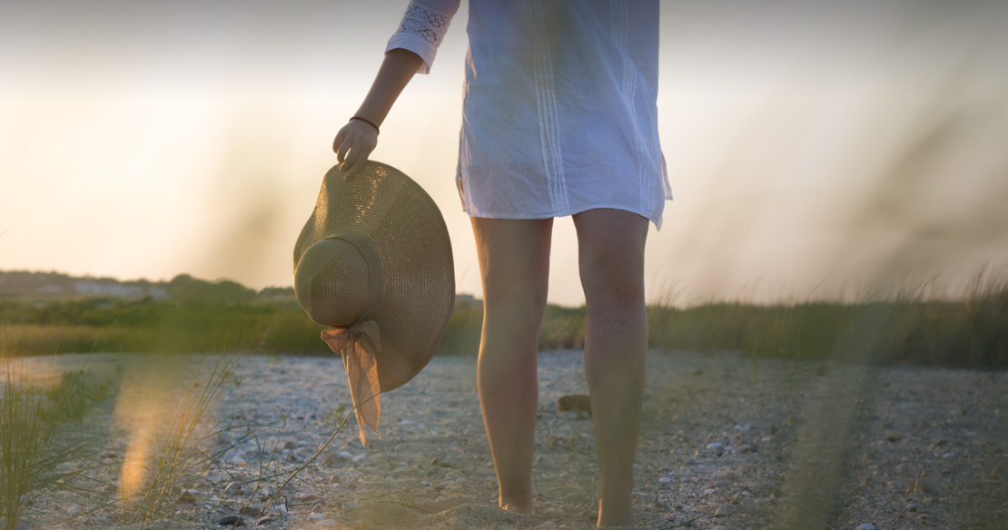 A woman walking on a beach on Martha's Vineyard holding her straw hat in her hand.