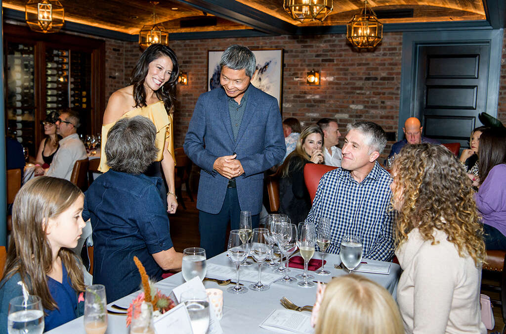 a woman in a yellow shirt and a man in a blue sports coat talking to a man and a woman at a dining room table