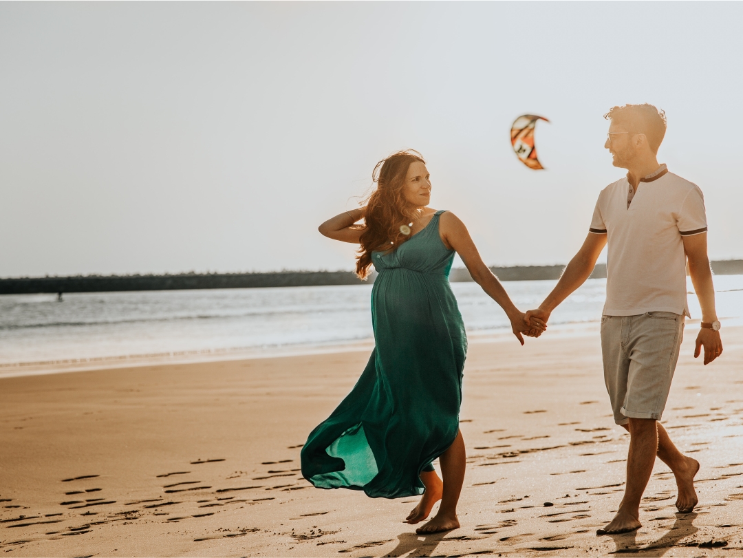 Husband and pregnant wife holding hands walking on the beach on Martha's Vineyard.