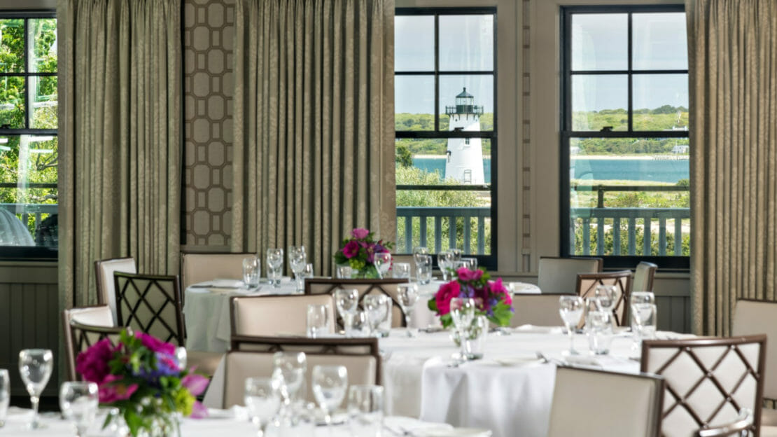 Dining room with view of the lighthouse and harbor set up with white table clothes and place settings and floral center pieces
