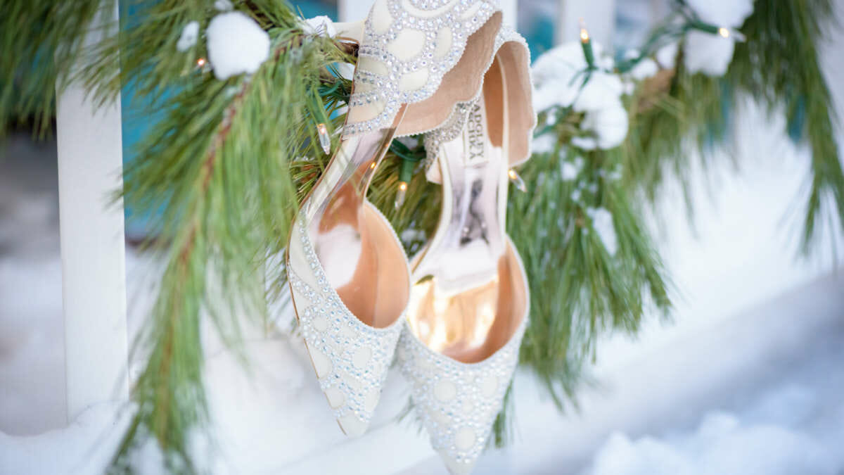 Close up photo of bride's wedding shoes hanging on garland in the winter at a Harbor View Hotel wedding.