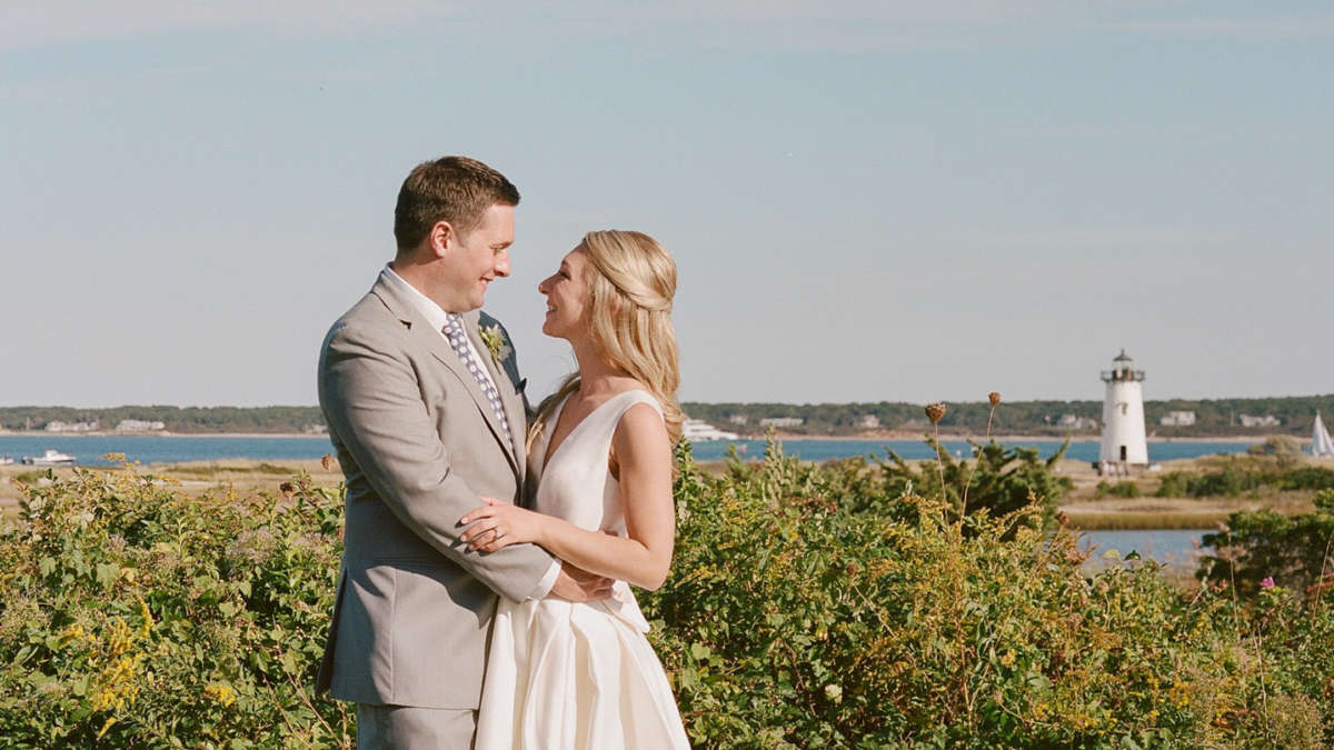 Bride and groom in front of Harbor View Hotel with the ocean and lighthouse in the background.