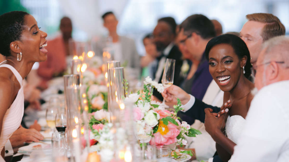 Bride and groom laughing at dinner table with guests