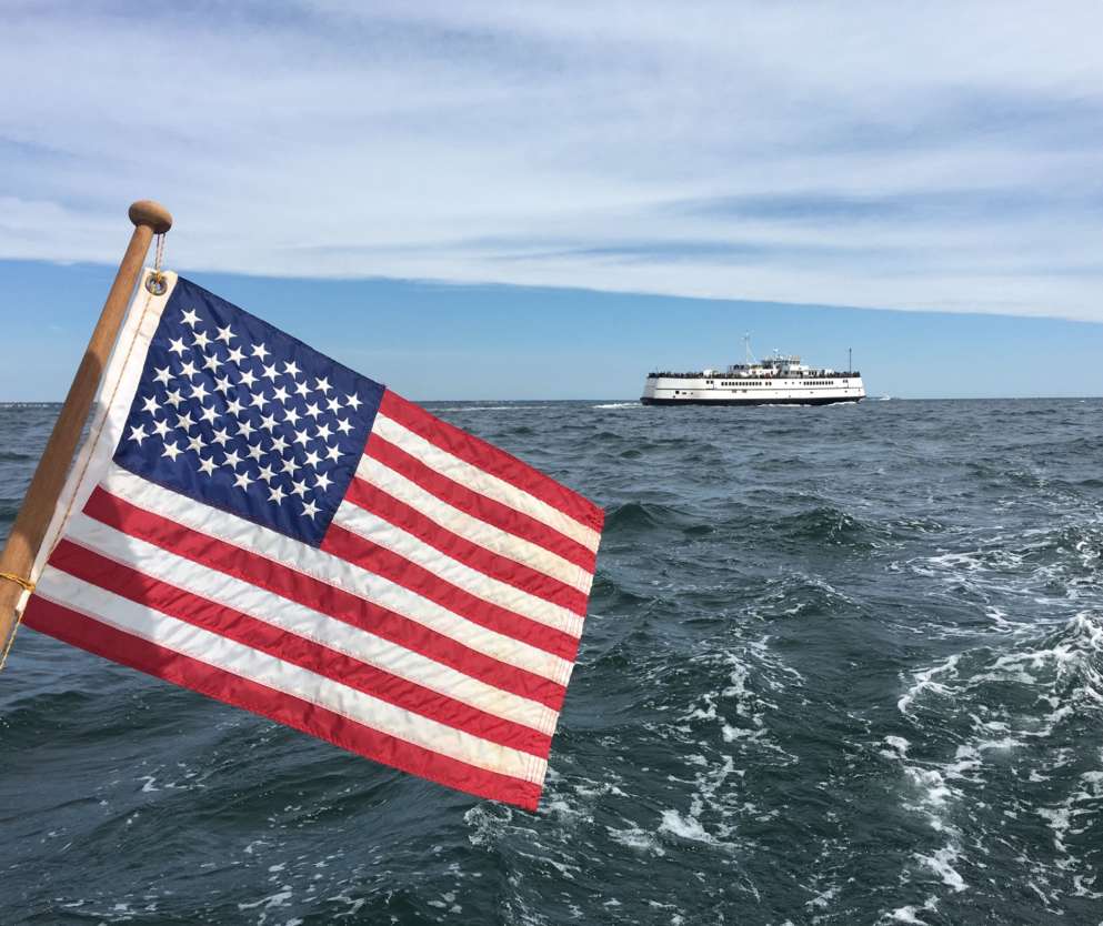 American flag on the back of a boat on the water with another boat in the background