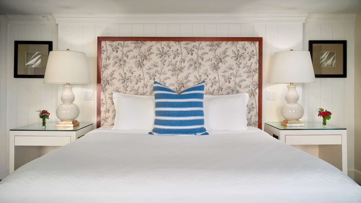 Queen bed with a blue and white pillow and two white side tables.