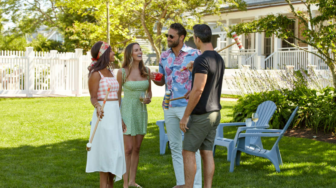 Two couples chatting with drinks playing croquet on the lawn