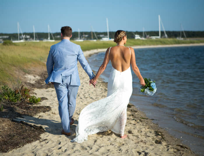 Bride and groom walking along lighthouse beach holding hands
