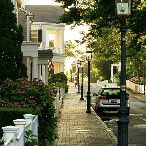 A quiet street on martha's Vineyard aligned with street lights and a car.