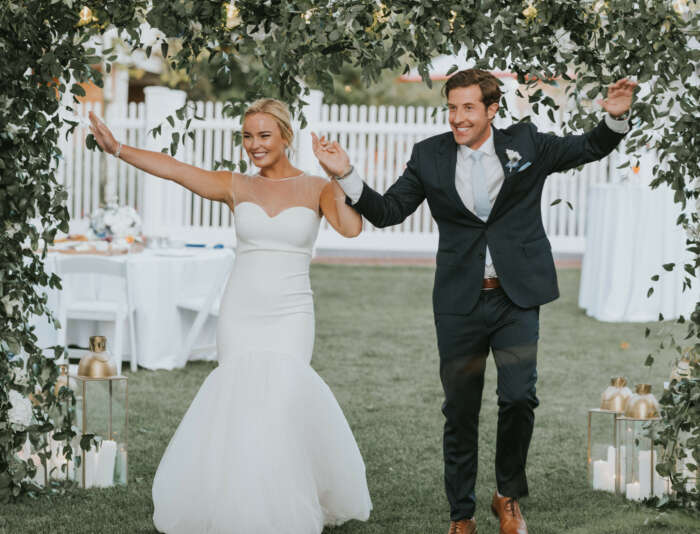 A bride and a groom smiling entering a wedding tent at Harbor View Hotel.