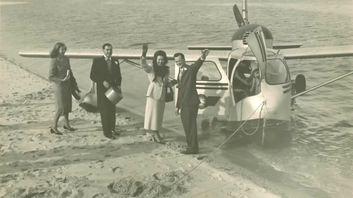 A black and white photo of people on a beach and a small airplane in the water