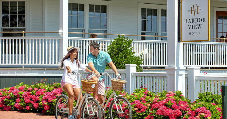 A man and a woman are looking at each other while riding a bike with baskets.