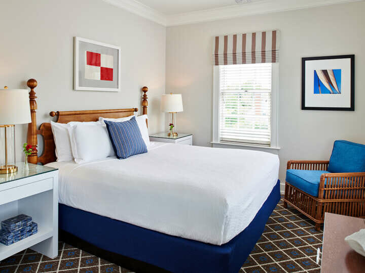 A queen size bed with white bedding and a blue chair.