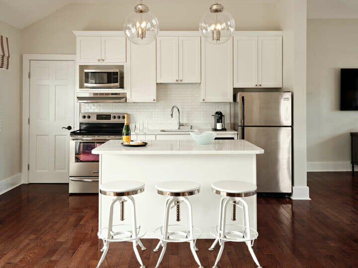 A kitchen with a white island, three stools, a silver fridge, and a stove.