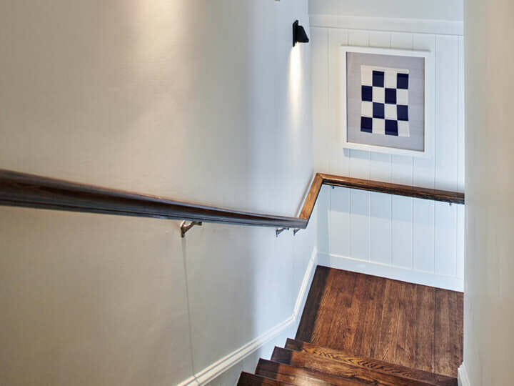 A staircase with brown hand rail and a blue and white checkered framed picture.