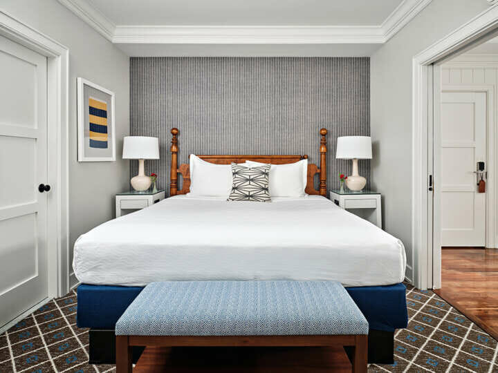 a bed with a white comforter, blue bench, and wallpaper behind the bed