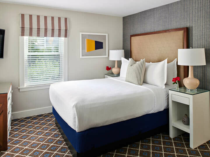 A bed with white bedding, a brown headboard, and a white nightstand.