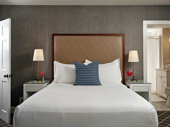 A bed with white bedding, a brown headboard, and a white nightstand.
