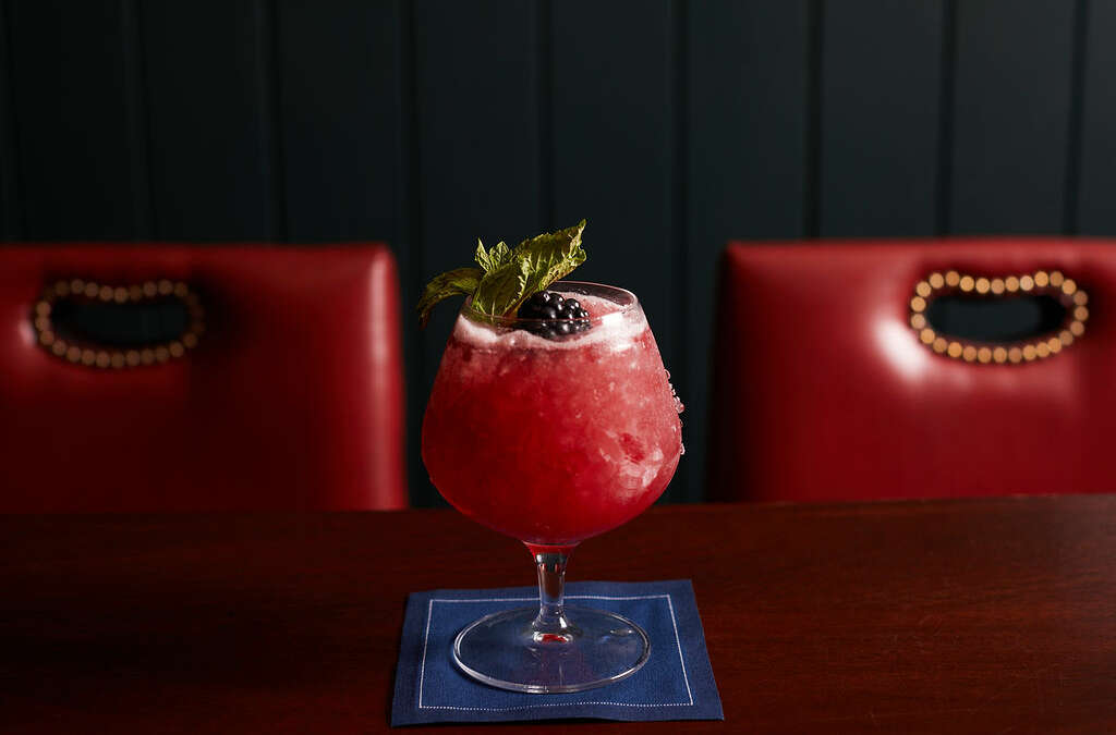a red cocktail with a mint leaf, and blackberry on a navy napkin
