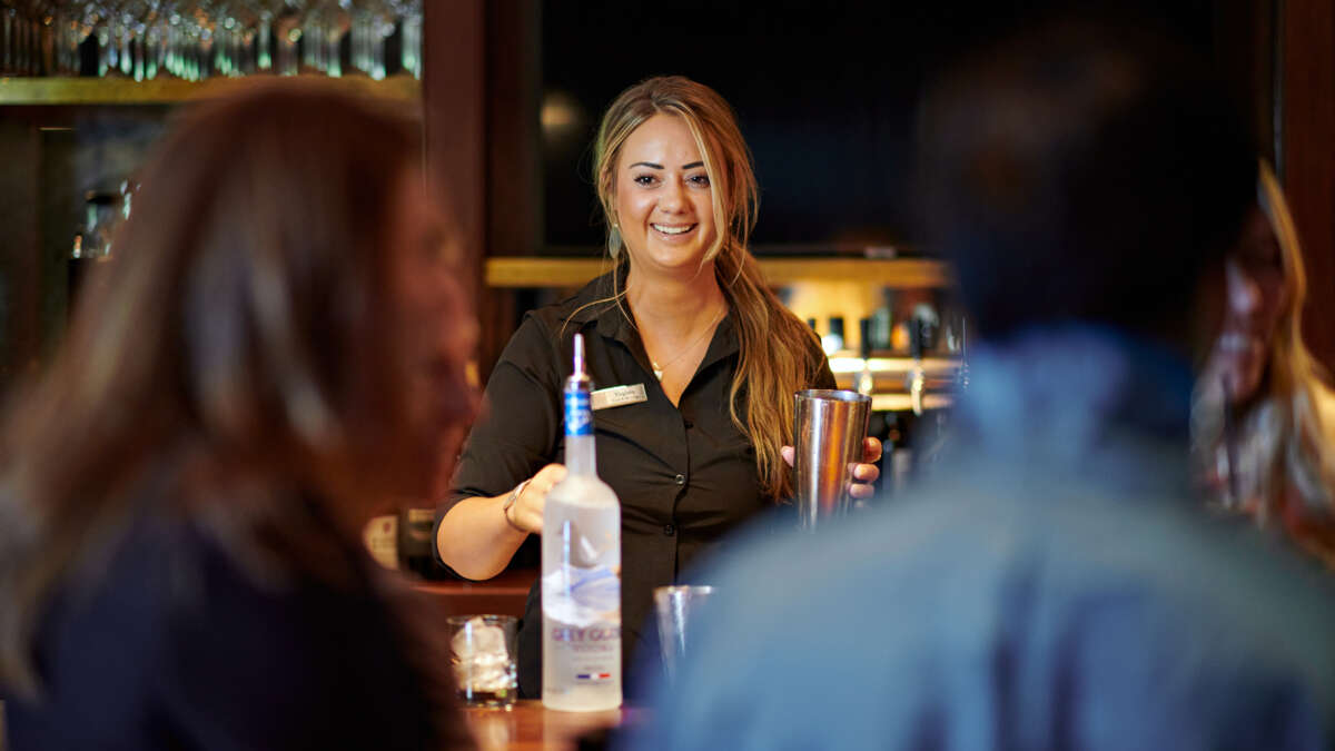 A smiling bartender pouring Grey Goose Vodka at The Clubhouse at Bettini Restaurant.