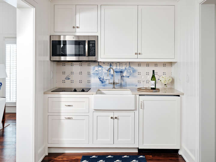 a kitchenette with white cabinets, a microwave, sink and a bottle of time