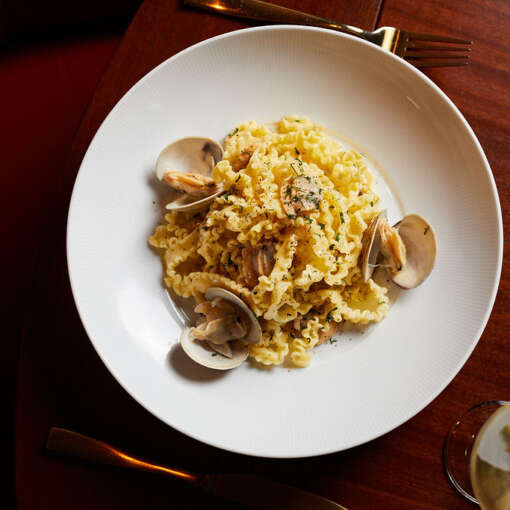 a white plate with a glass of white wine and pasta and clams