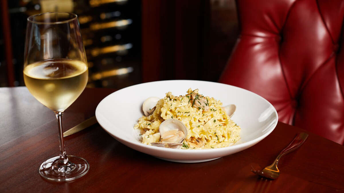a glass of white wine, a white plate with pasta and clams