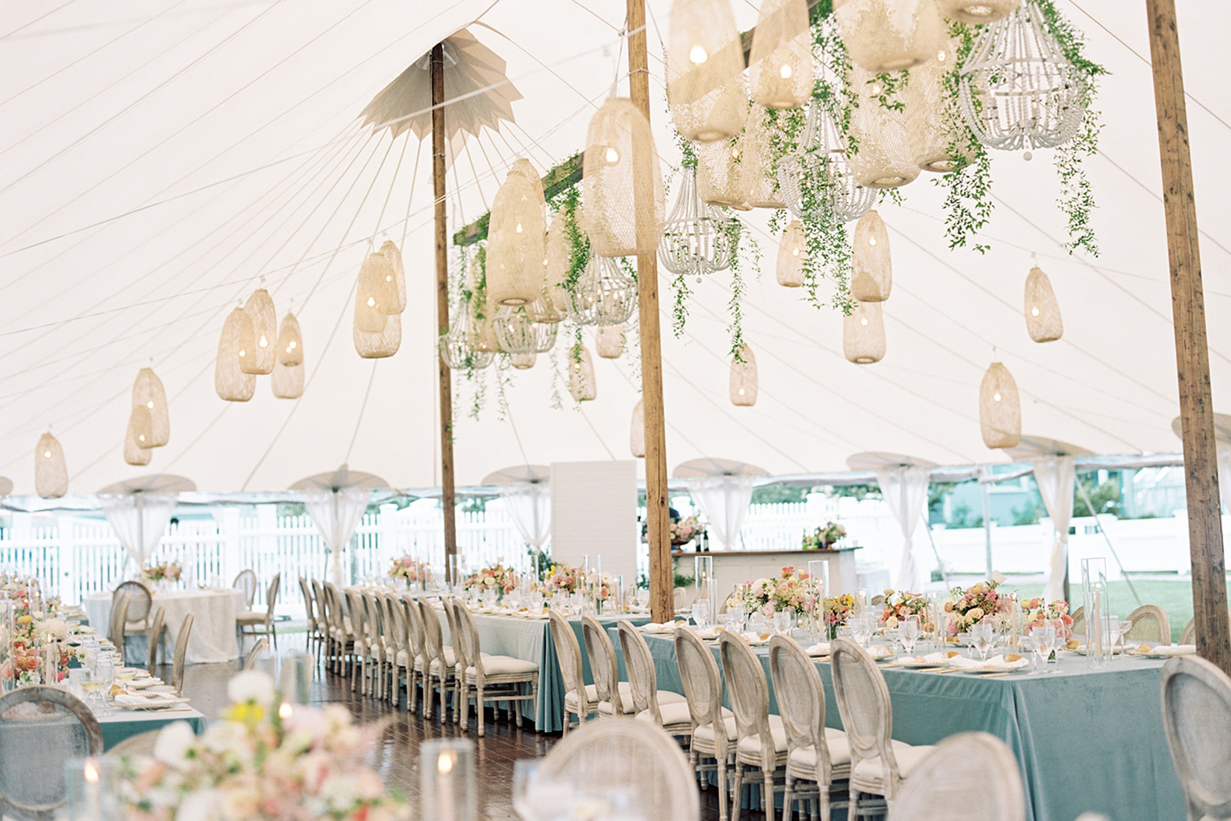 A wedding tent with lighting handing and tables with a blue table cloth and flowers in center.