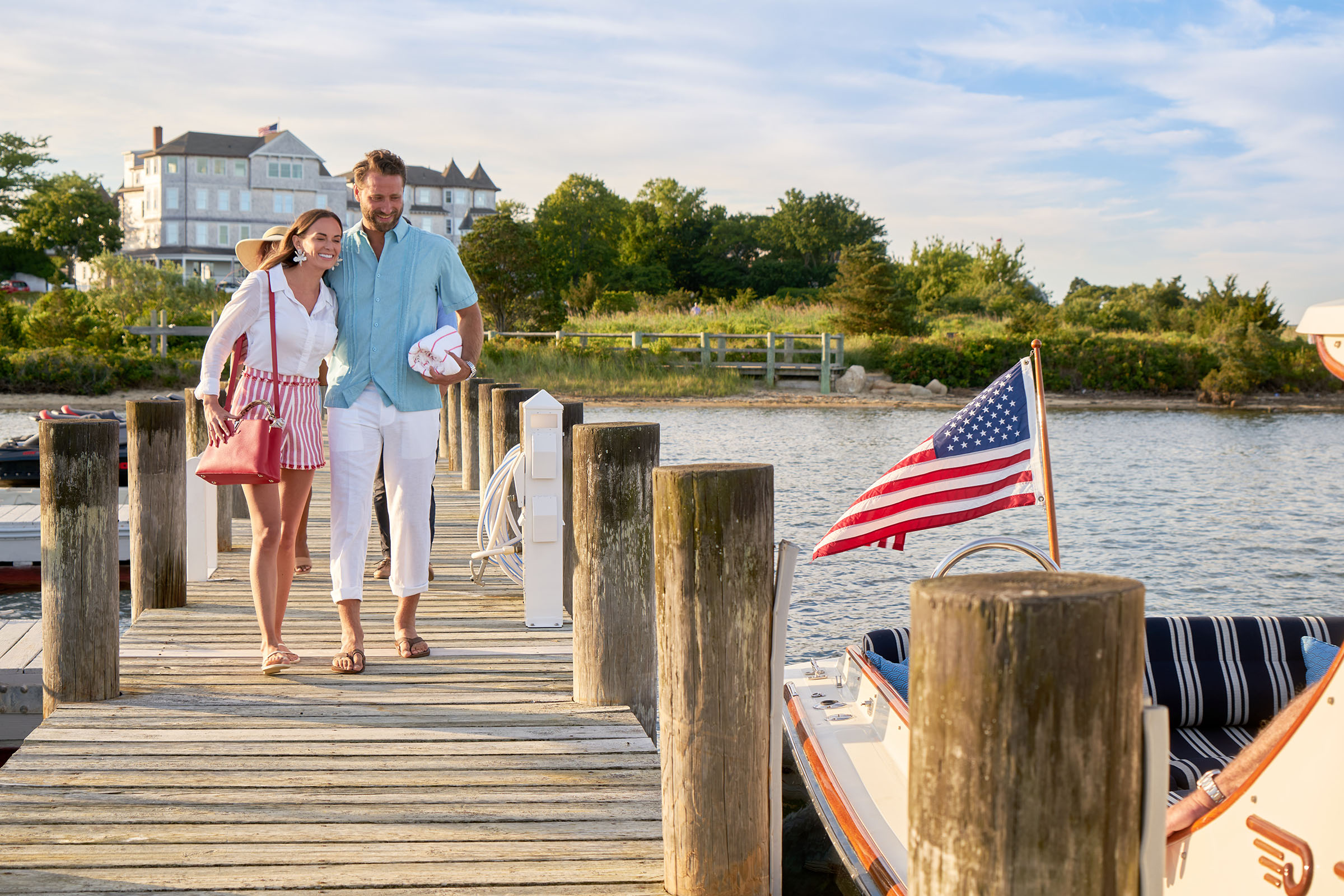 A smiling woman and a man walking on a tan dock to a boat with a USA flag.