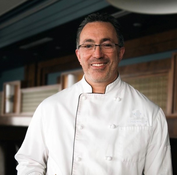 A man wearing glasses wearing a white chef's coat.