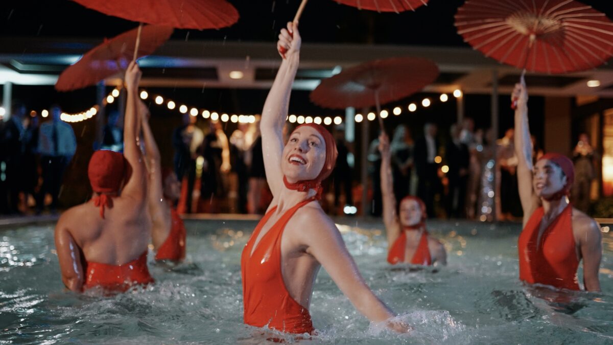 Aqualillies performers in the pool dancing with red bathing suits and umbrellas.