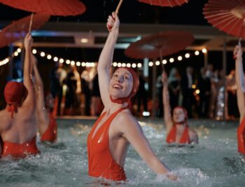 Aqualillies performers in the pool dancing with red bathing suits and umbrellas.